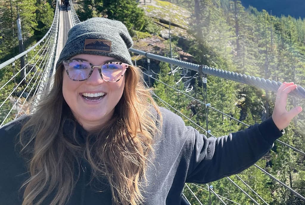 A smiling young woman in a toque on a suspension bridge