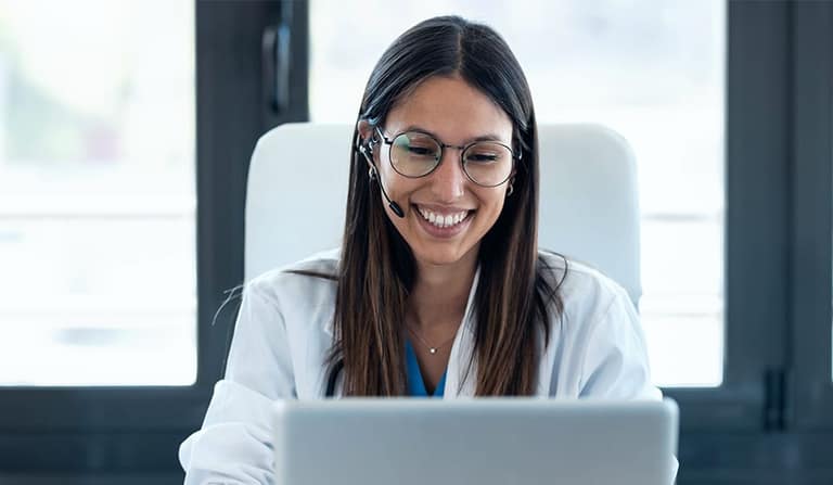 A smiling doctor at a laptop in a bright office