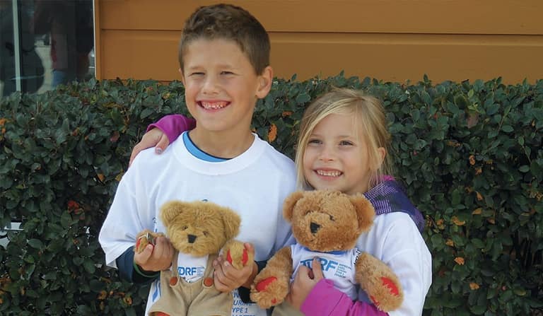 Two smiling children holding Breakthrough T1D teddy bears