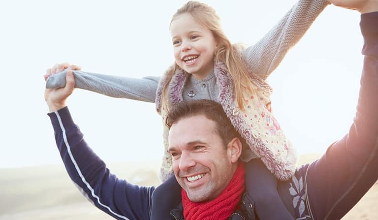 A father carrying his laughing daughter on his shoulders