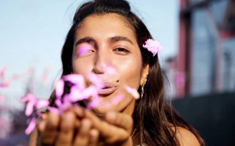 A young woman smiling and blowing flower petals from her hands