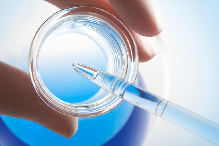 A pipette above a dish of blue cell culture