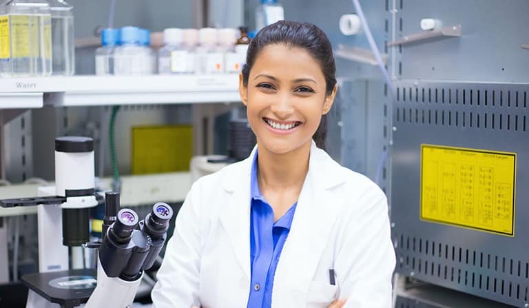 A smiling researcher in a lab coat at a microscope